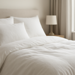 a close-up of a neatly made bed with white lightweight bedding, pillows, and a bedside lamp, suggesting a cool and breat