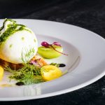 A ball of fresh mozzarella atop a colorful salad with tomatoes and herbs.