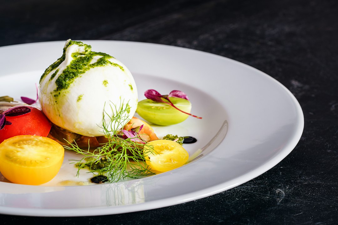 A ball of fresh mozzarella atop a colorful salad with tomatoes and herbs.